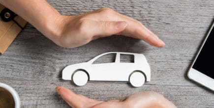 Hands protecting icon of car over wooden table. Top view of hands showing gesture of protecting car. Car insurance and automotive business concept.