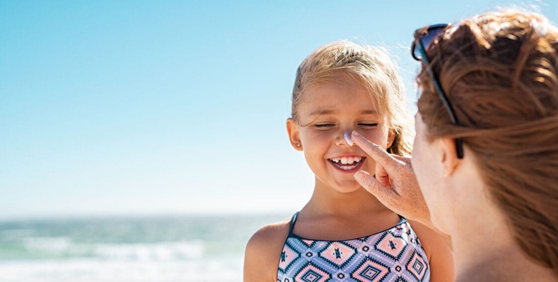 mother applying suntan lotion to daughter's face to stay safe in heat