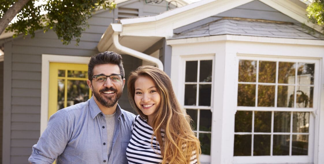 Portrait Of Excited Couple Standing Outside New Home