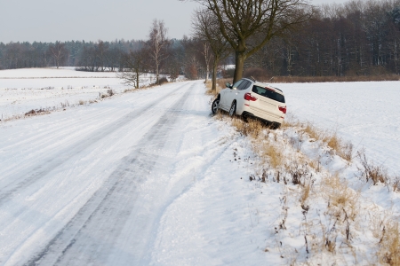 white suv crashed in a country road kerbside due to slippery road covered in snow with skid marks