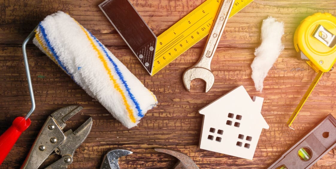 Mini white house laying on table surrounded by tools for home maintenance concept