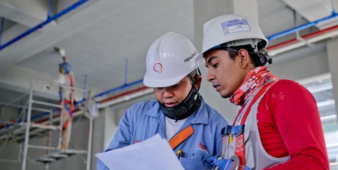 Two people wearing hard hats are reading an article about the top 5 OSHA violations of 2021 to better prepare for their future working endeavors.