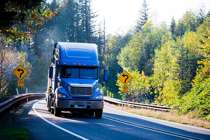 Blue semi truck and flat bed trailer on sunny green and gold autumn trees