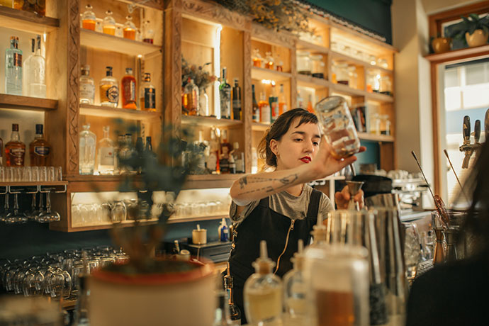 Young female bartender pouring cocktails behind a bar counter