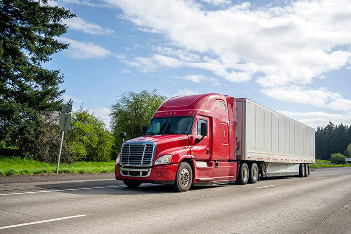 Red big rig popular bonnet semi truck transporting commercial cargo in dry van semi trailer moving on the straight wide highway