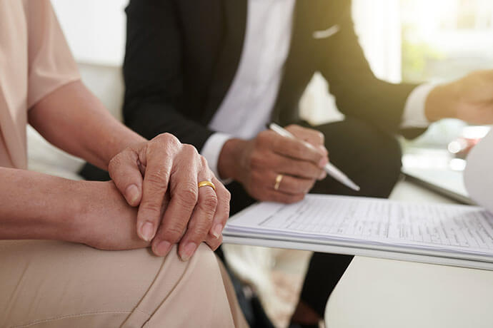 Hands of senior woman letting agent to fill life insurance policy document with her personal data