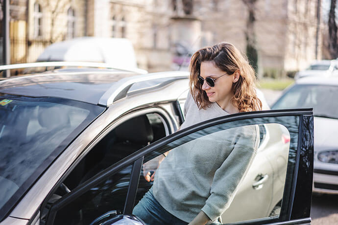 Happy cheerful young woman in sunglasses getting into her car on a city street