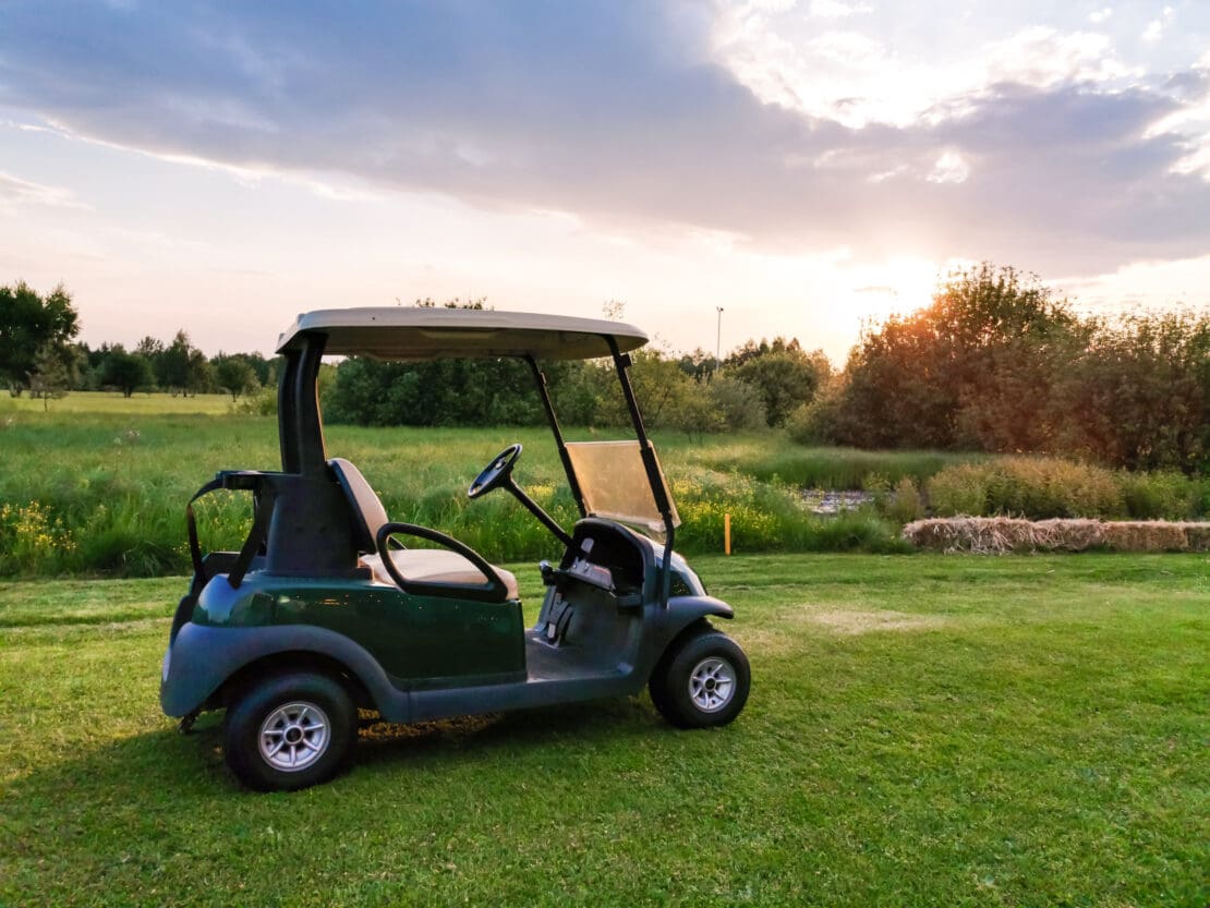 A golf cart sits on a golf course. There is no driver in the cart.
