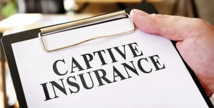 A person is holding a clipboard. The board is holding a piece of paper that says "Captive Insurance"