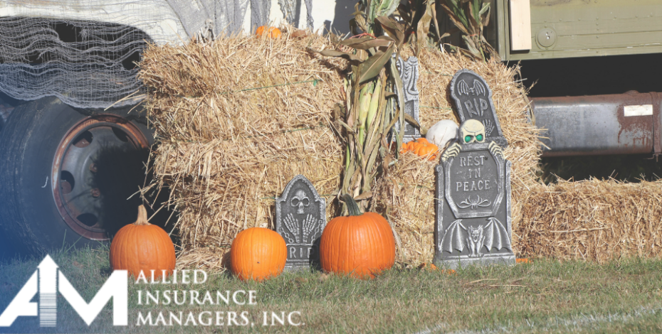 A tractor by a stack of hay. There are three pumpkins and halloween decorations in front of the hay stack
