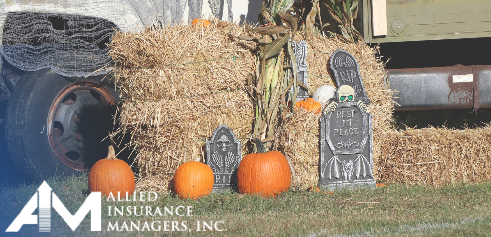 A tractor by a stack of hay. There are three pumpkins and halloween decorations in front of the hay stack