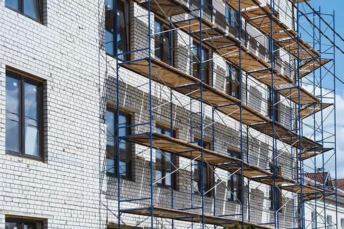 Multi-level blue metal scaffolding with wooden platforms erected against white brick apartment building under construction.